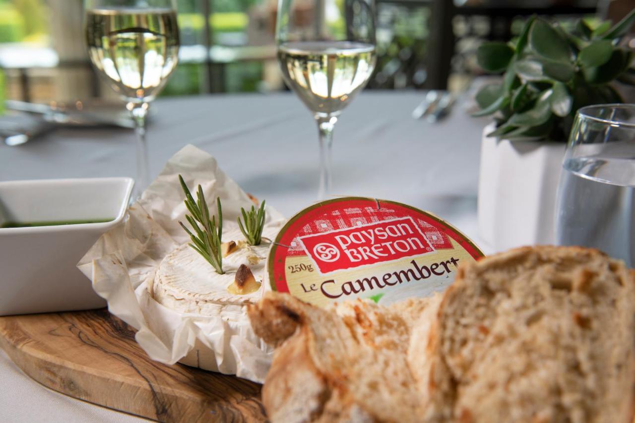 Macdonald Bath Spa Hotel Kültér fotó The photo features a dining setting that includes a wooden platter with a round Camembert cheese, garnished with fresh rosemary sprigs. Nearby, there is a serving of bread, likely sliced, and a small bowl, potentially for dipping or spreading. In the