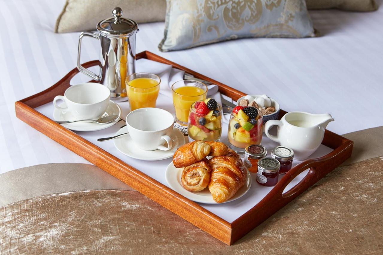 Macdonald Bath Spa Hotel Kültér fotó The photo shows a wooden tray arranged with a delightful breakfast spread. On the tray, there are two cups, a coffee pot, and several glasses of orange juice. There's also a small bowl of mixed fruit, featuring various colorful pieces. Additionally, 