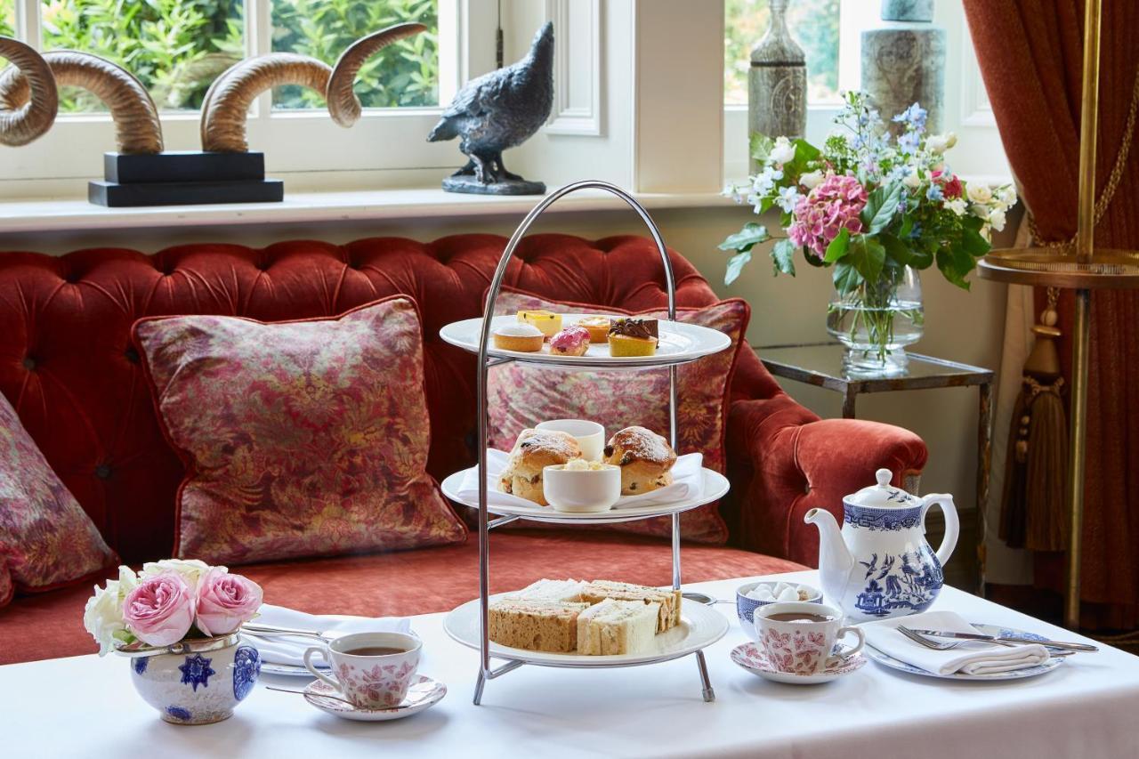 Macdonald Bath Spa Hotel Kültér fotó The photo showcases an elegant afternoon tea setting. In the foreground, there is a three-tiered serving stand filled with various pastries and scones, including some topped with cream and fruit. Surrounding the stand is a beautifully arranged table 