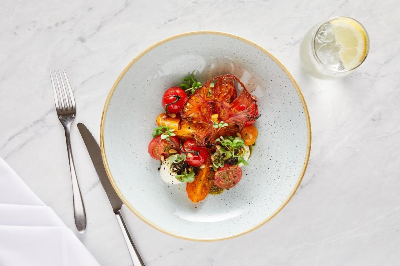 Macdonald Bath Spa Hotel Kültér fotó The photo shows a beautifully arranged plate of food. The dish features a mix of colorful ingredients, including roasted or grilled vegetables, likely bell peppers and tomatoes, along with fresh greens. There are also some circular slices of another 