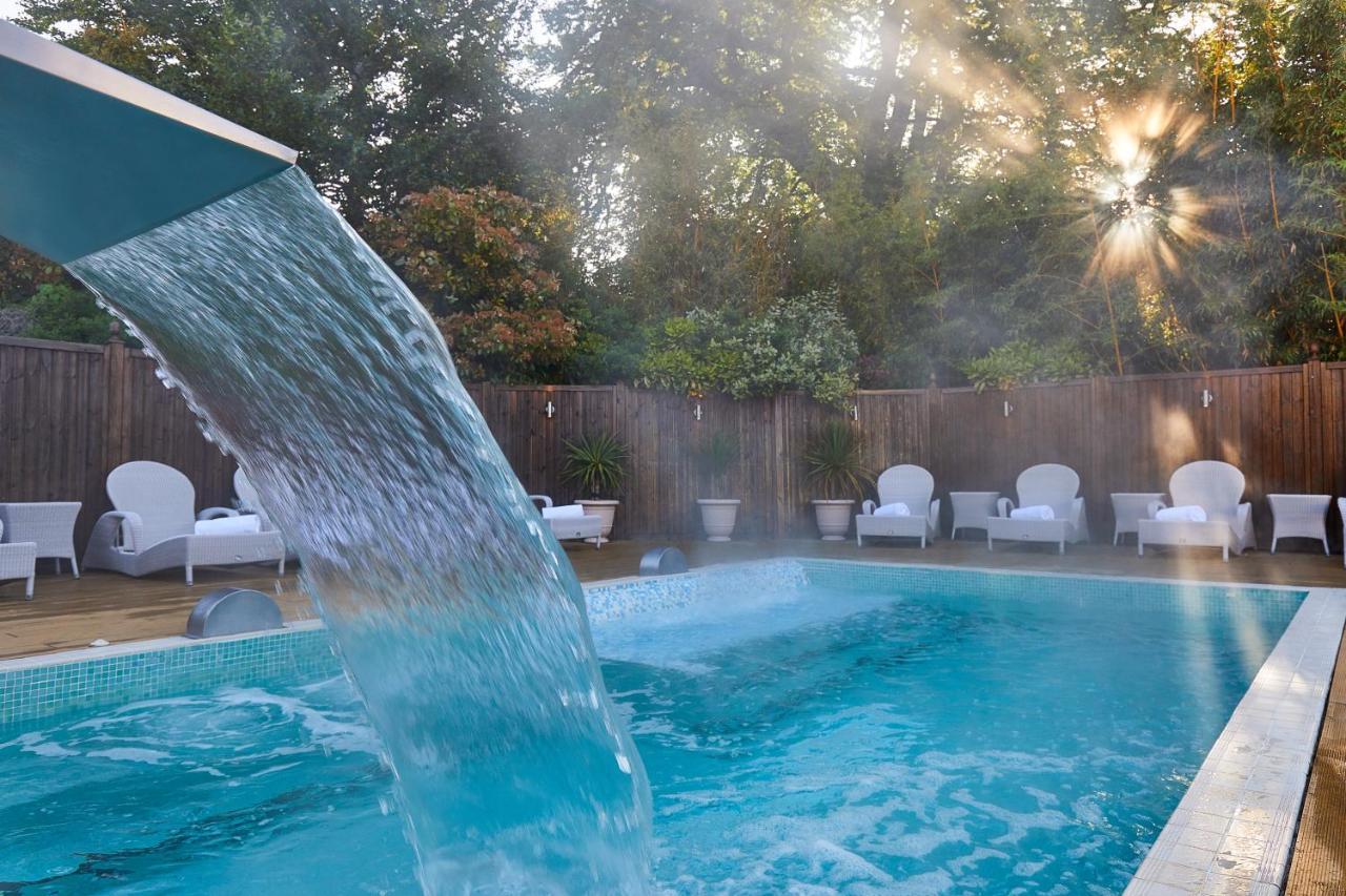 Macdonald Bath Spa Hotel Kültér fotó The photo shows a tranquil swimming pool surrounded by greenery. Water is cascading from a feature into the pool, creating a refreshing effect. In the background, there are white lounge chairs positioned neatly along the poolside, inviting relaxation
