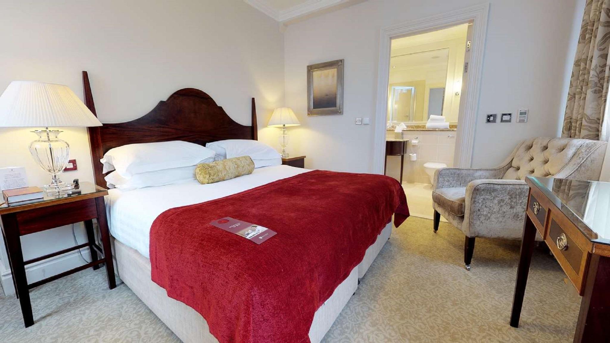 Macdonald Bath Spa Hotel Kültér fotó The photo shows a well-furnished hotel room. In the center, there is a large bed with white linens and a red throw blanket. A decorative pillow is placed on the bed. On either side of the bed, there are bedside tables with lamps. To the right, there 