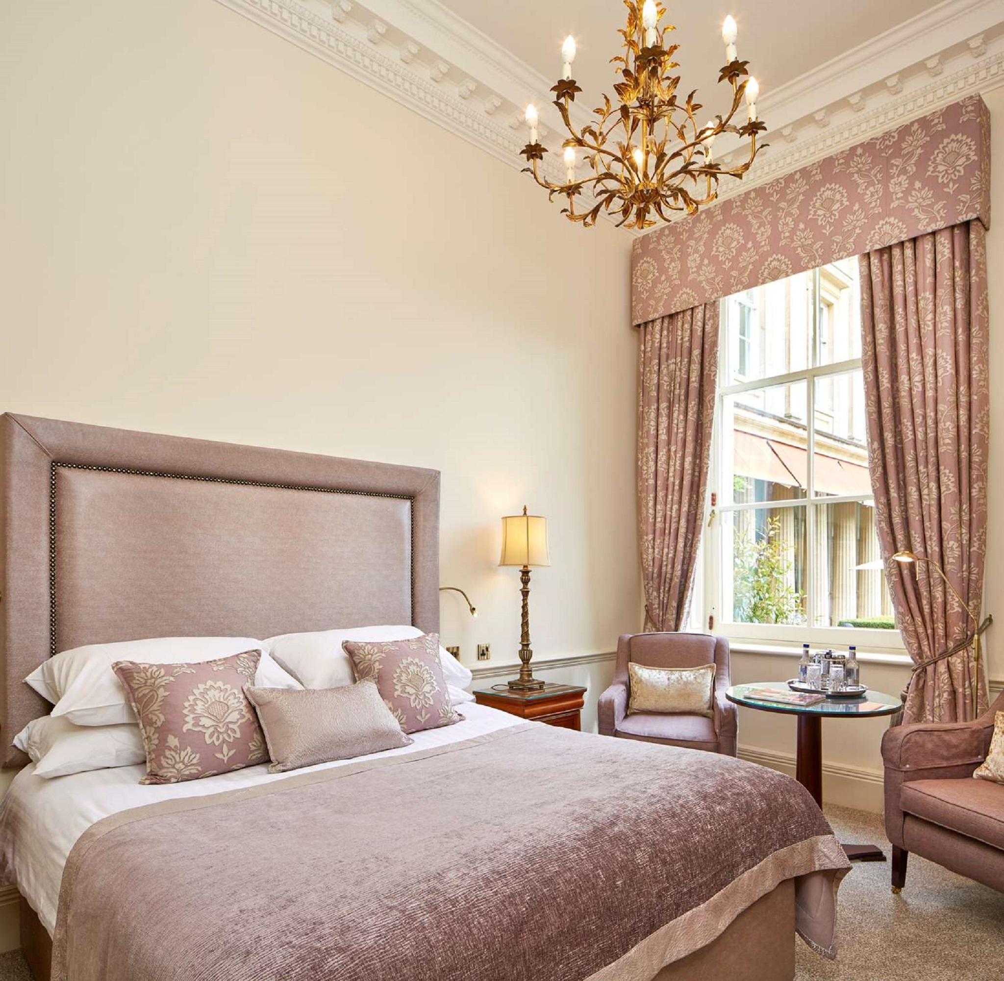 Macdonald Bath Spa Hotel Kültér fotó The photo shows a beautifully decorated hotel room. It features a large bed with a plush headboard, adorned with several decorative pillows. The walls are painted in a soft color, and there is a chandelier hanging from the ceiling. Natural light come