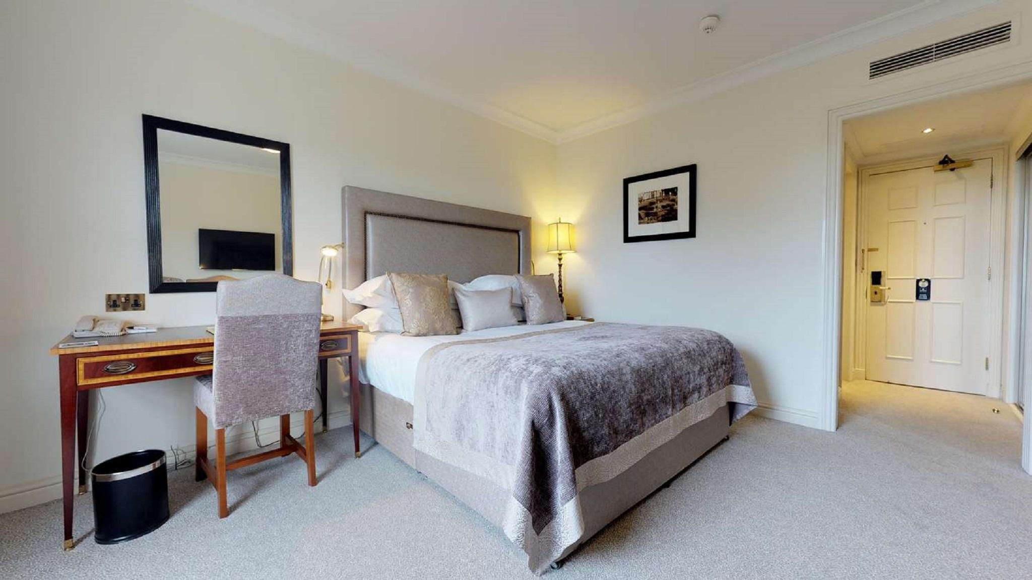 Macdonald Bath Spa Hotel Kültér fotó The photo shows a well-decorated hotel room. In the center, there's a comfortable bed with plush bedding and decorative pillows. A bedside table with a lamp is positioned next to the bed. To the left, there's a small desk with a chair, accompanied by