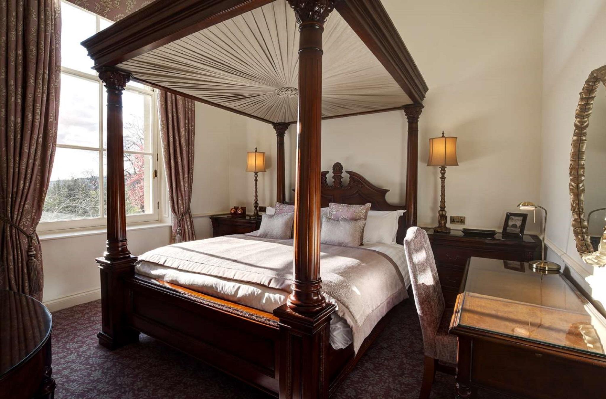 Macdonald Bath Spa Hotel Kültér fotó The photo shows a well-decorated bedroom featuring a four-poster bed with an elegant wooden frame. The bed is dressed with light-colored linens and several decorative pillows. On either side of the bed, there are matching bedside lamps that provide s