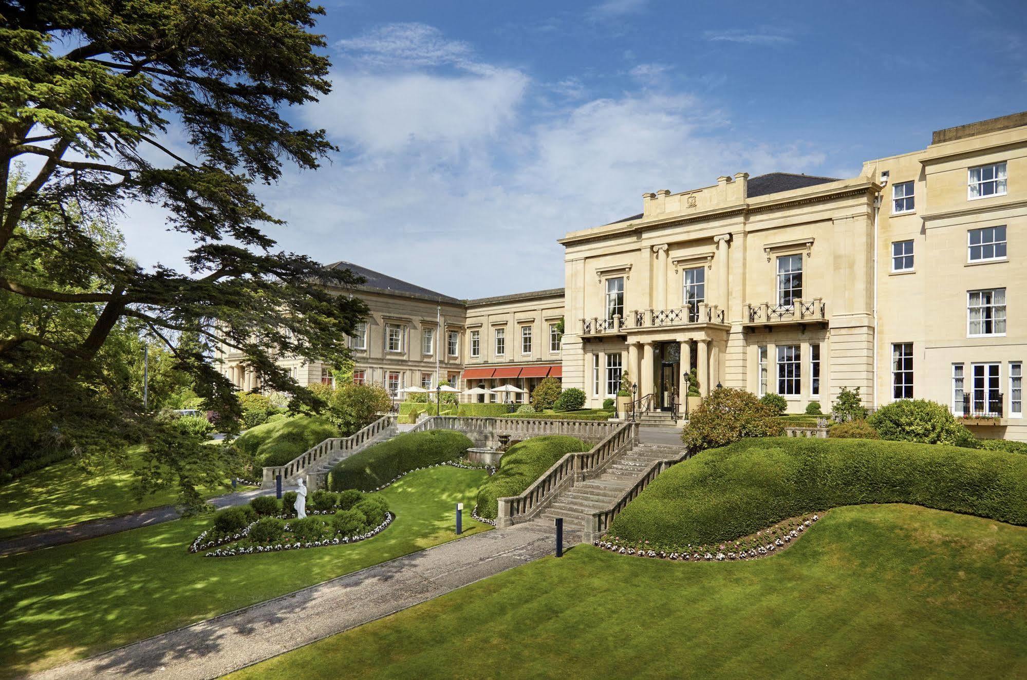 Macdonald Bath Spa Hotel Kültér fotó The photo shows a grand building, likely a hotel or estate, surrounded by well-manicured gardens and lawns. The architecture appears elegant, with multiple stories and large windows. There are steps leading up to the entrance, and the setting include